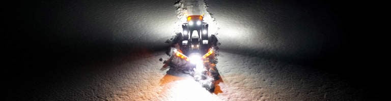 Traktor och plog på väg med snö