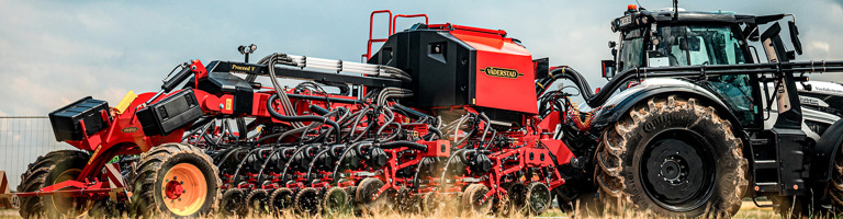 Röd såmaskin som dras av en vit traktor. Såmaskinen är en Väderstad Proceed och traktorn en Valtra.