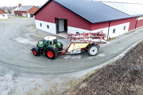 En Fendt-traktor kör med en växtskyddsspruta på en gårdsplan. Sprutan är en Hardi Commander Twin